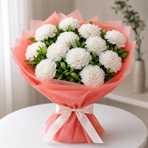 Bouquet of white flowers wrapped in pink paper with a white ribbon on a white surface.