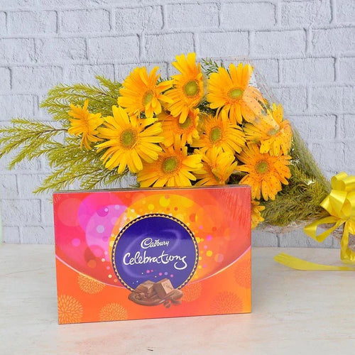 Bouquet of yellow flowers with a Cadbury Celebrations chocolate box on a light gray surface.