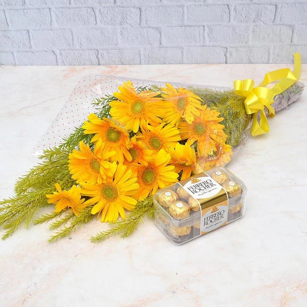 Bouquet of yellow flowers with a box of Ferrero Rocher chocolates on a light surface.