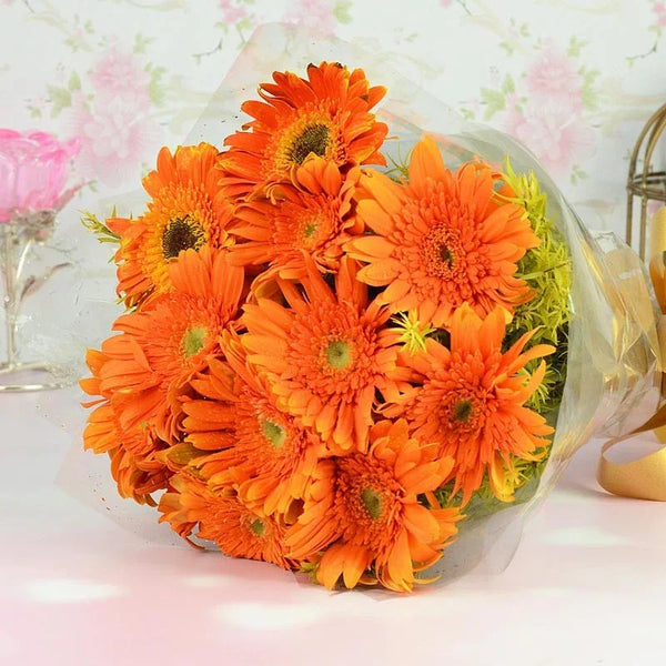 Bouquet of bright orange flowers with green centers, wrapped in clear plastic on a light background.