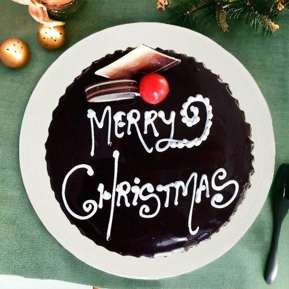 Chocolate Merry Christmas cake with festive decoration on white plate, green background
