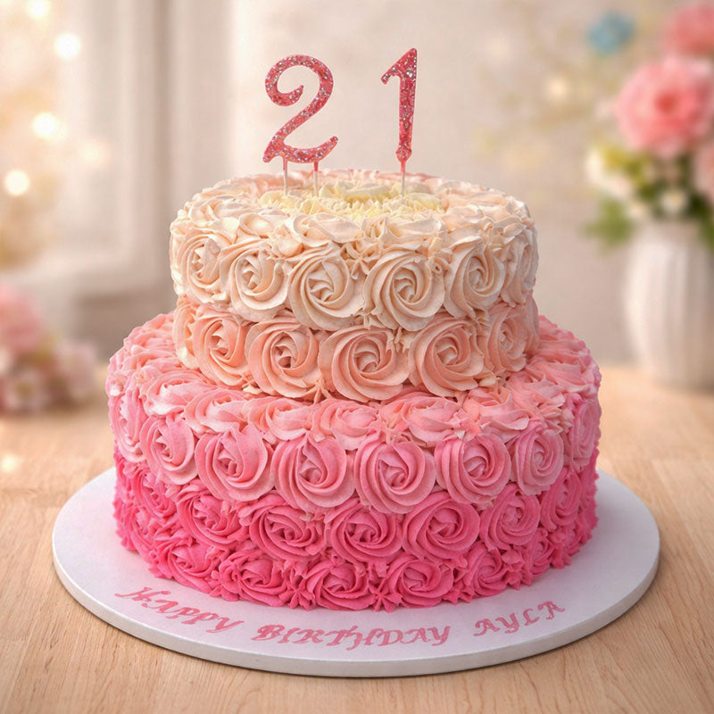 Two-tiered pink birthday cake with 'Happy Birthday Ayla' on a table.