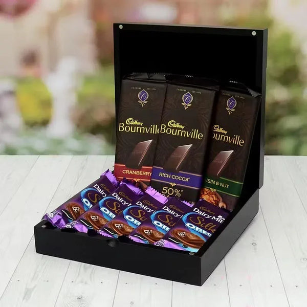 Display of Cadbury Bournville and Dairy Milk chocolate bars on a wooden surface with a blurred outdoor background.