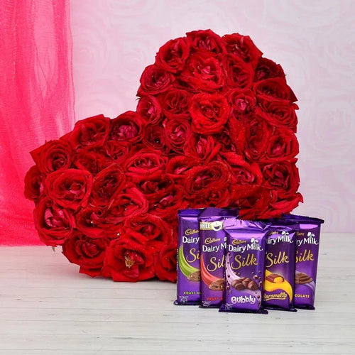 Heart-shaped arrangement of red roses with Cadbury Dairy Milk Silk chocolate bars on a pink and white background