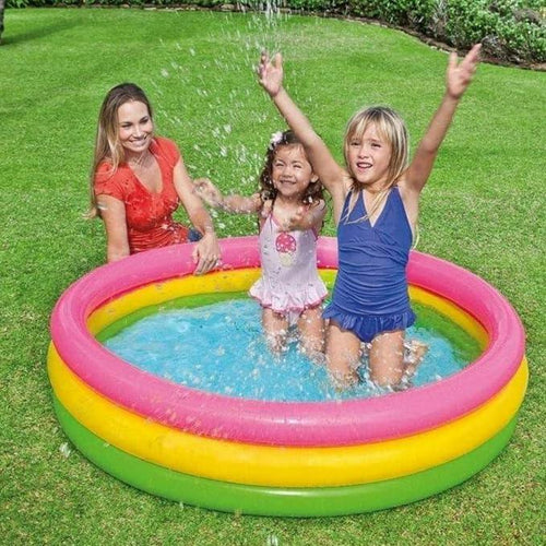 Three children playing in a colorful inflatable pool on a grassy area.