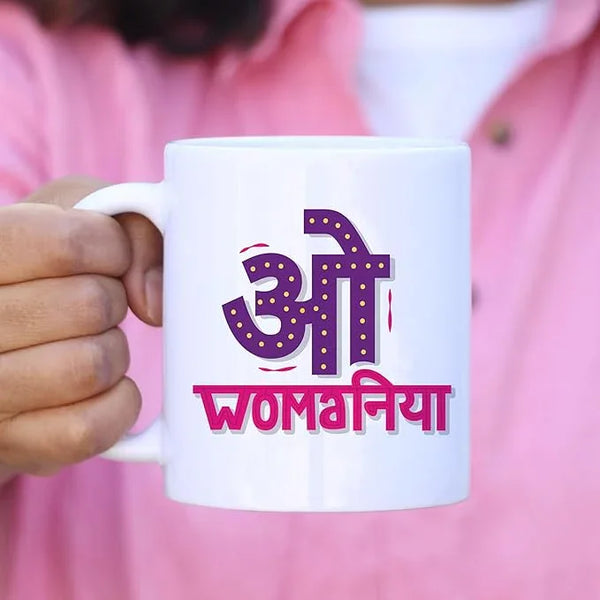 White mug with purple and pink text held by a person wearing a pink shirt.