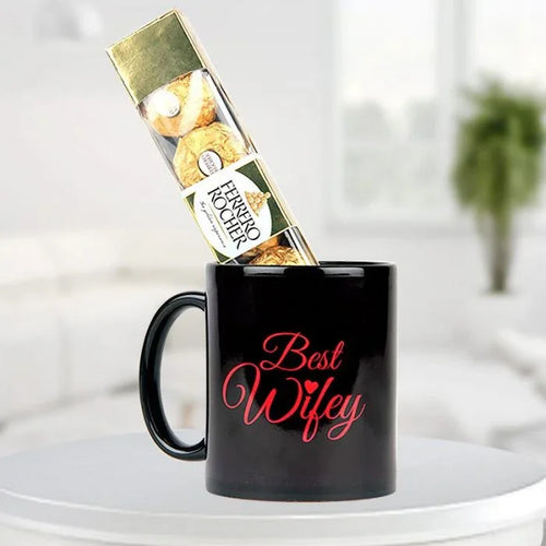 Black mug with 'Best Wifey' text, Ferrero Rocher chocolate, on a white surface.