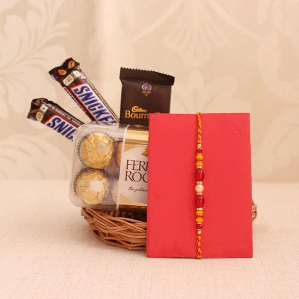 Basket of assorted chocolates including Ferrero Rocher and Snickers, with a red envelope featuring gold ribbons on a beige background.