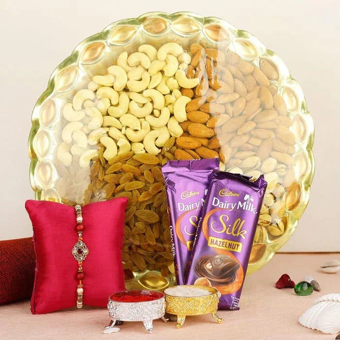 Assorted dry fruits in a decorative bowl with Cadbury Dairy Milk Silk chocolate bars and a red pillow with jewelry on a beige background.