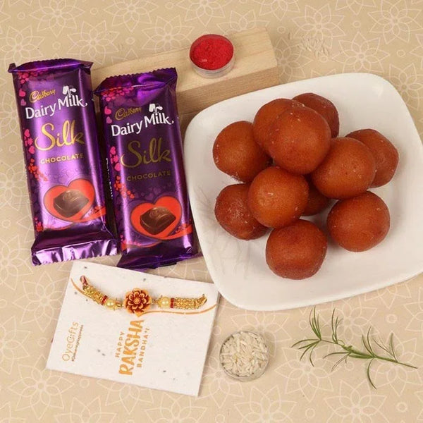 Two Cadbury Dairy Milk Silk chocolate bars, a plate of round brown sweets, and a Raksha Bandhan card on a beige background.