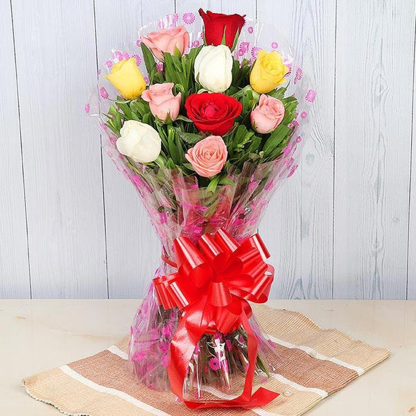 Bouquet of multicolored roses with a red bow on a wooden surface.