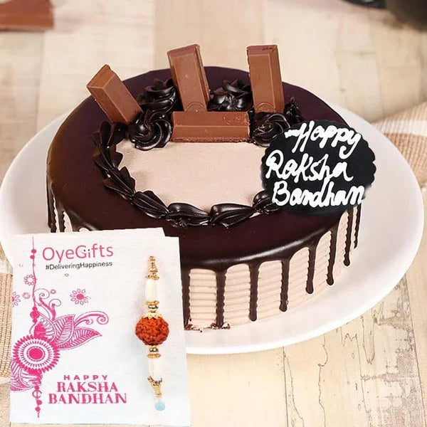 Chocolate cake with 'Happy Raksha Bandhan' decoration, accompanied by a Rakhi and card on a table.