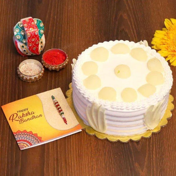 White cake with yellow dots, Raksha Bandhan card, and decorative items on a wooden surface