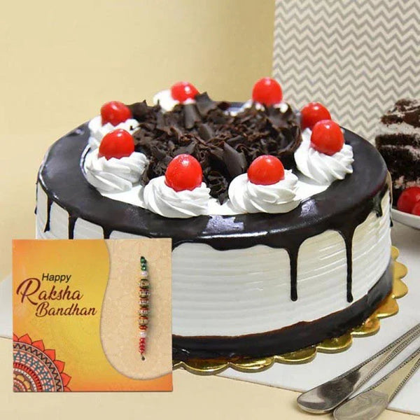 Chocolate cake with white frosting and red cherries, accompanied by a 'Happy Raksha Bandhan' card and rakhi.
