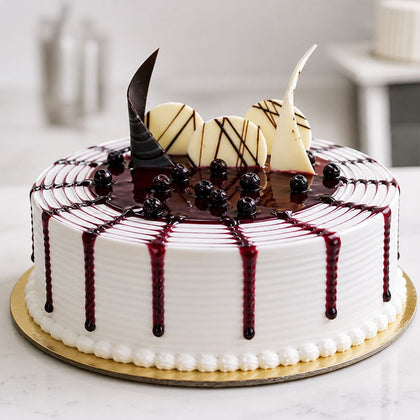 Decorative cake with white frosting, dark drizzle, and fruit on a marble surface.