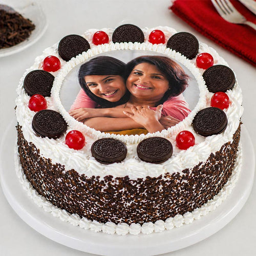 Chocolate cake with white frosting, cherries, and Oreo cookies, featuring a photo of two women on the cake.