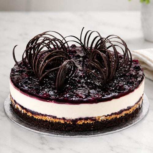 Layered cake with blueberry topping and chocolate decorations on a marble surface