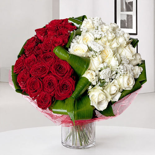 Bouquet of red and white roses in a clear vase on a white surface.