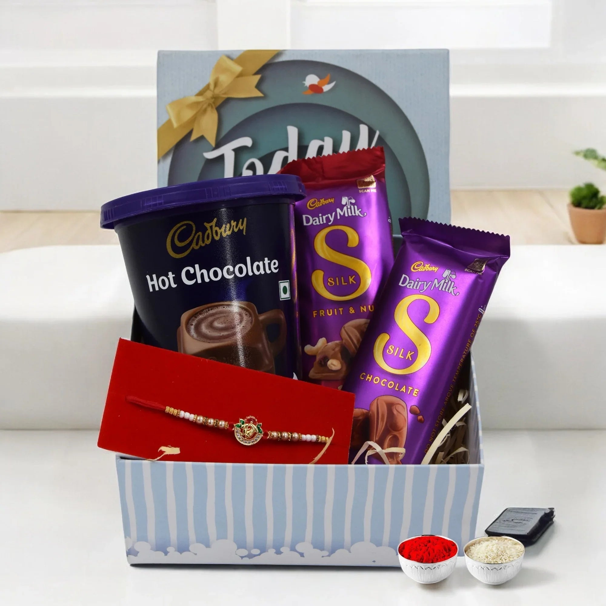 Gift basket with Cadbury Dairy Milk chocolate bars and hot chocolate in a blue striped box.