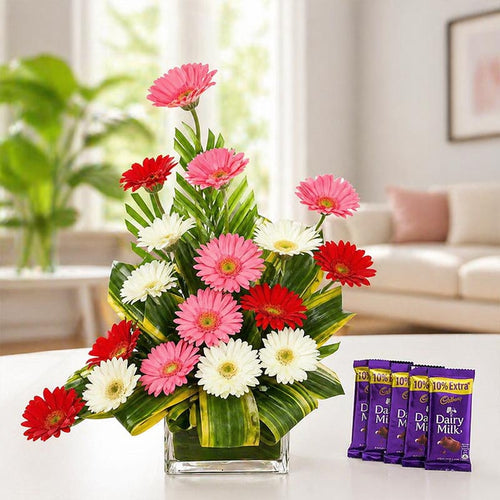 Bouquet of colorful flowers in a glass vase with Dairy Milk chocolate bars on a table.