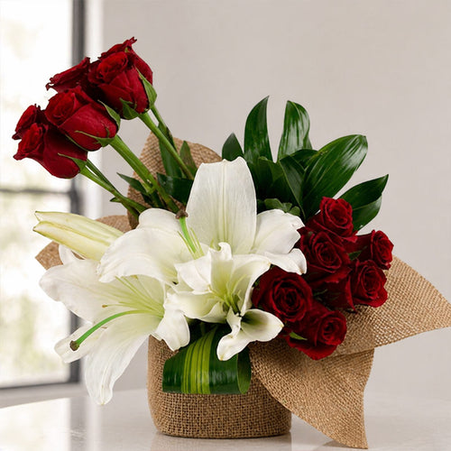 Bouquet of red roses and white lilies in a woven basket on a light surface.