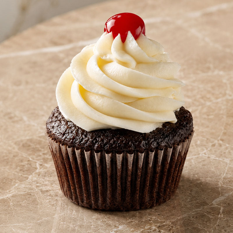 Chocolate cupcake with white frosting and a red cherry on top, placed on a marble surface.