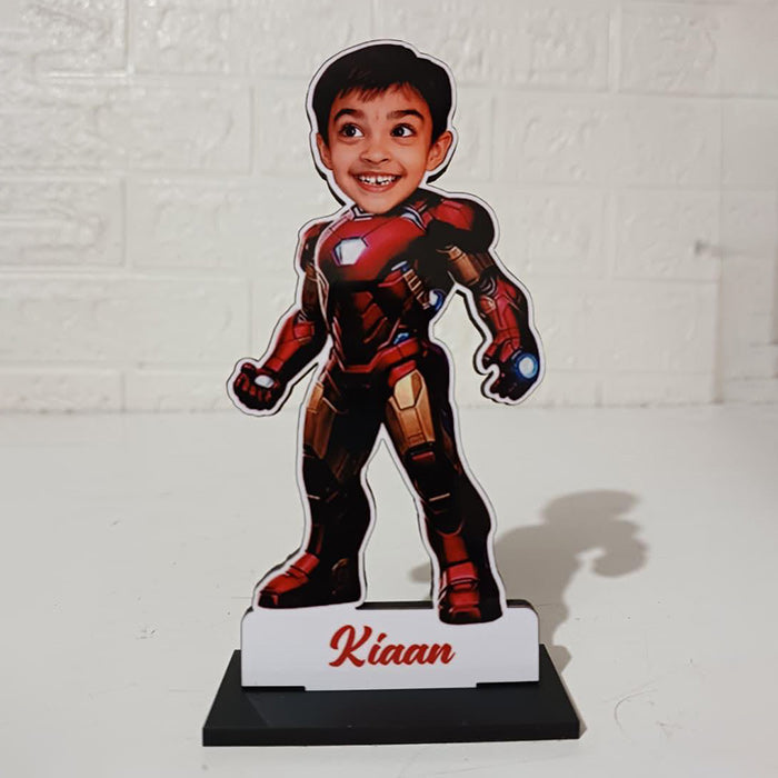 Cardboard cutout of a child in superhero costume with 'Kiaan' on a stand against a white brick wall.