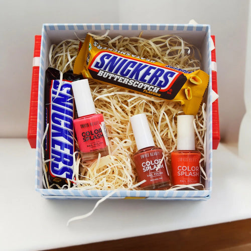 Box with Snickers candy bars and nail polish bottles on a white surface