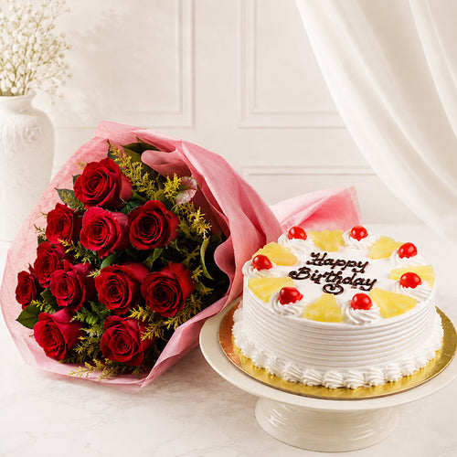 Bouquet of red roses and a birthday cake with pineapple slices on a white surface.