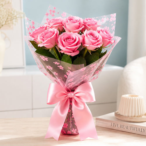 Bouquet of pink roses wrapped in cellophane with a pink bow on a light surface.