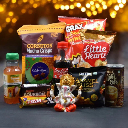 Assorted snacks and drinks with a small statue of Ganesha on a dark surface with a blurred light background.