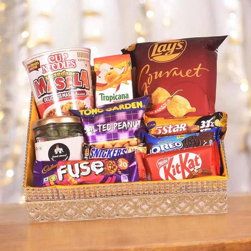 Assorted snack items including chips, candies, and drinks in a decorative basket with a blurred background.