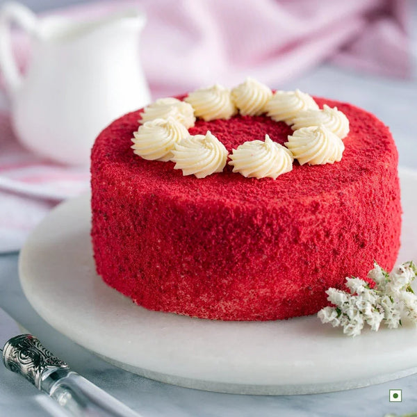 Eggless red velvet cake with cream swirls on top, displayed on a marble platter