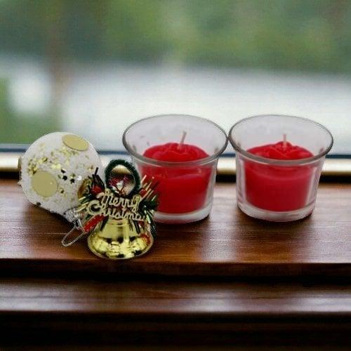 Red candles in glass holders with a Christmas ornament on a wooden surface