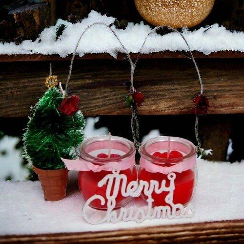 Mini Christmas tree and two red candles in jars with 'Merry Christmas' sign on snow.