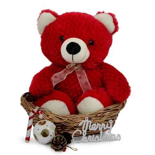 Red teddy bear in a wicker basket with Christmas decorations and a Merry Christmas sign