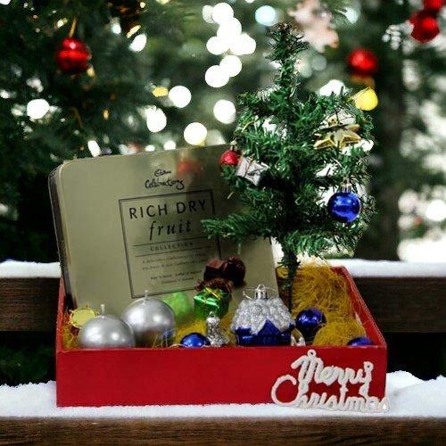 Christmas gift hamper with dry fruits, mini decorated Christmas tree, and festive ornaments in a red box.