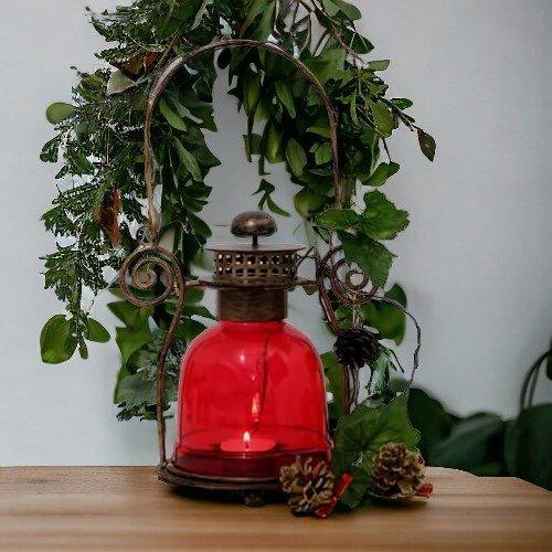 Red vintage lantern with candle, pinecones, and green foliage on wooden table