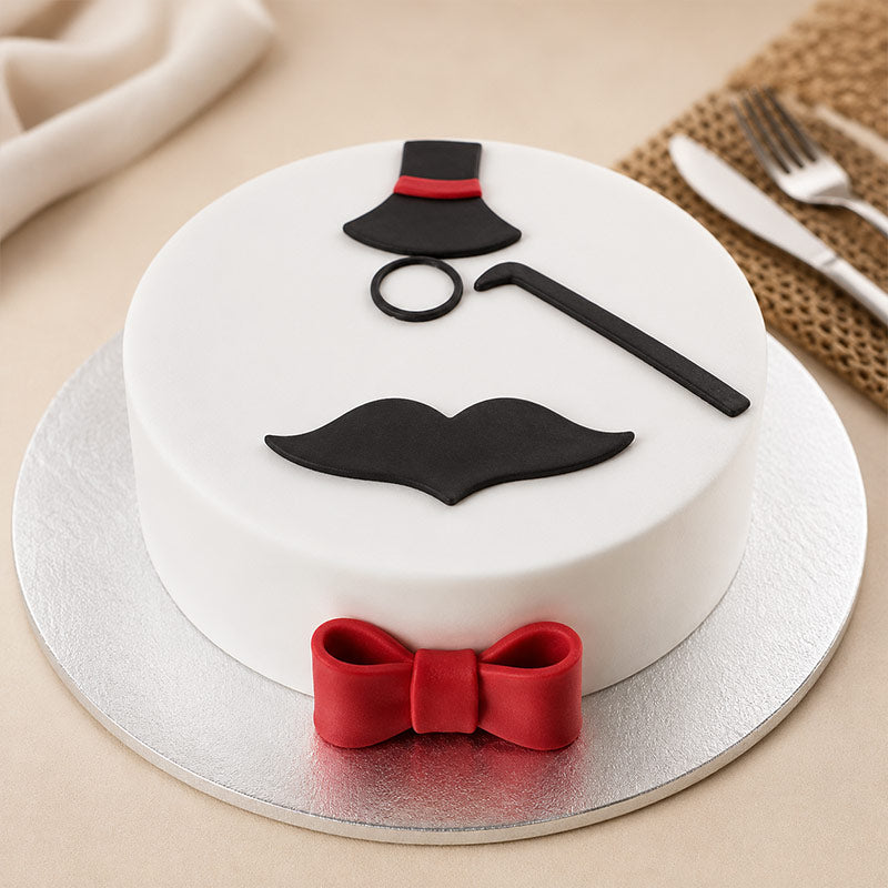White cake with black top hat, mustache, and red bow tie on a beige surface.