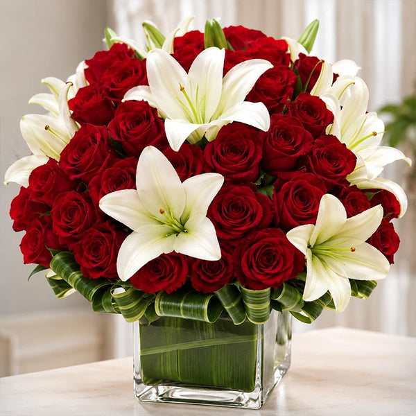 Bouquet of red roses and white lilies in a clear vase on a light surface.