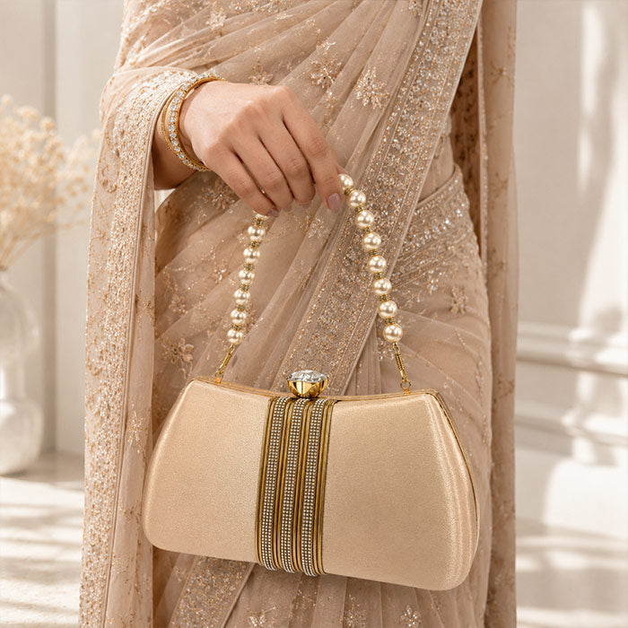 Beige handbag with pearl handle held by a person in a matching saree.