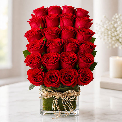 Bouquet of red roses in a clear vase with a decorative bow on a light background