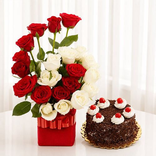 Bouquet of red and white roses in a red vase next to a chocolate cake with red berries on a white background