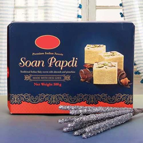 Box of Soan Papdi Indian sweets with almonds and pistachios, festive gift sticks beside