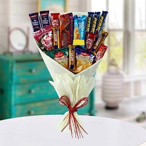 Bouquet of assorted chocolate bars tied with a red ribbon on a white surface.