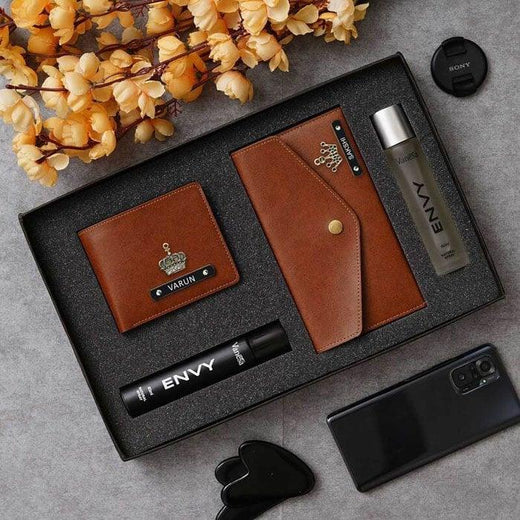 Gift set with brown leather wallet, black and silver bottle, and phone on a gray surface with yellow flowers.