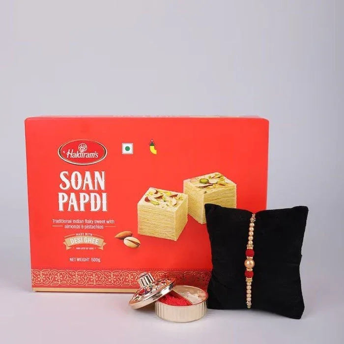 Haldiram's Soan Papdi box with a black pillow and decorative items on a gray background