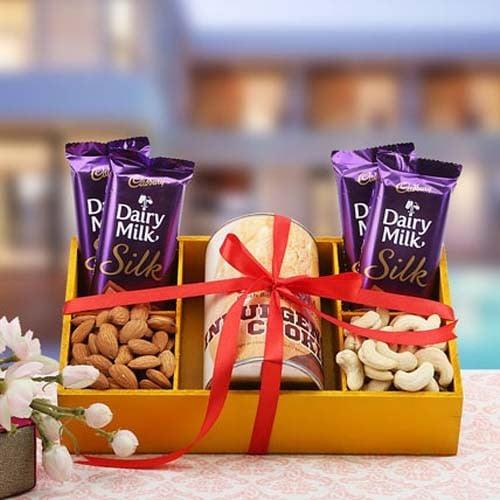 Gift box with Dairy Milk Silk chocolates, almonds, cashews, and a printed mug, wrapped with a red ribbon.