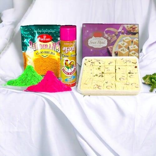 Holi gift hamper with snacks, sweets, colors, and gulal powder on white fabric