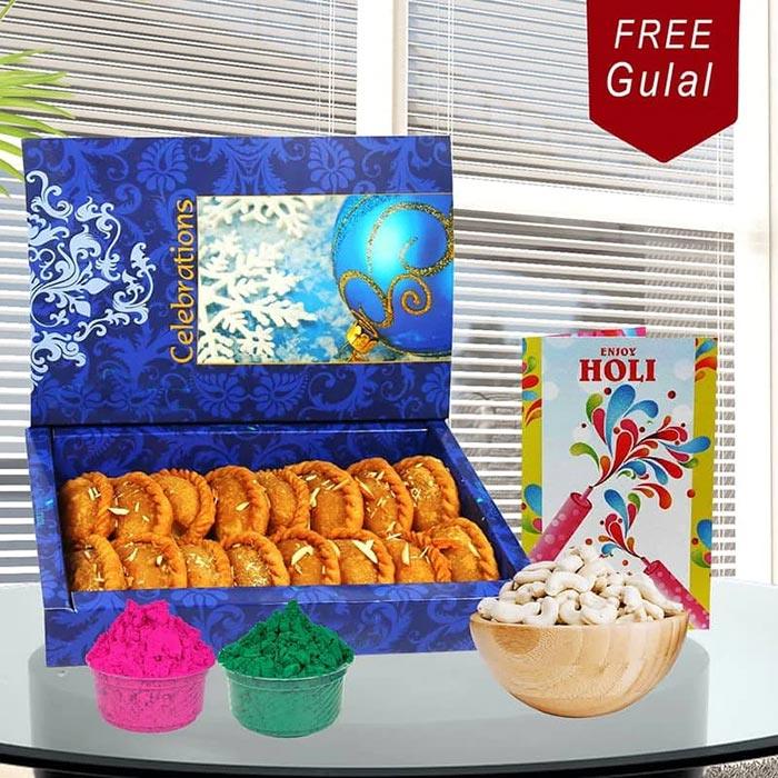 Gulab jamun in a decorative box with Holi-themed items on a table.